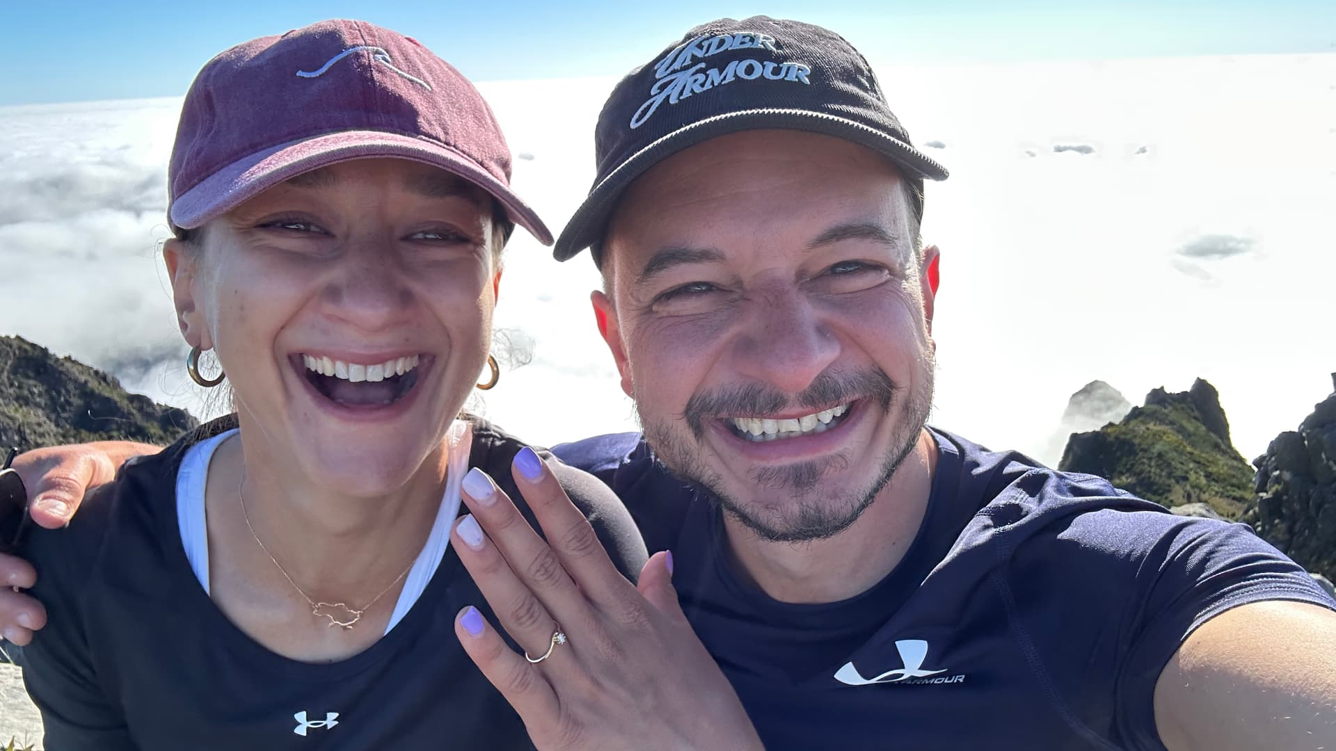 Olya and Andrei above the clouds on a mountain top, showing the engagement ring