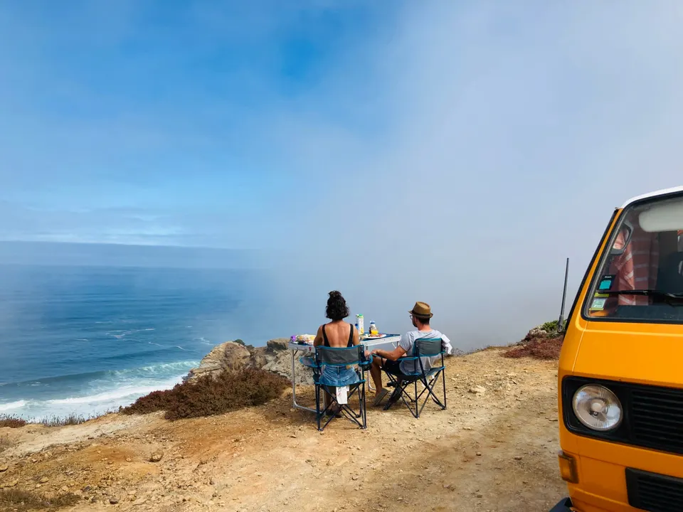 Breakfast laid out on a folding table on a cliff above the Atlantic, beside an orange camper van